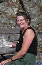 A woman in green pants and a black tank top sitting on a bench with a mossy rock background